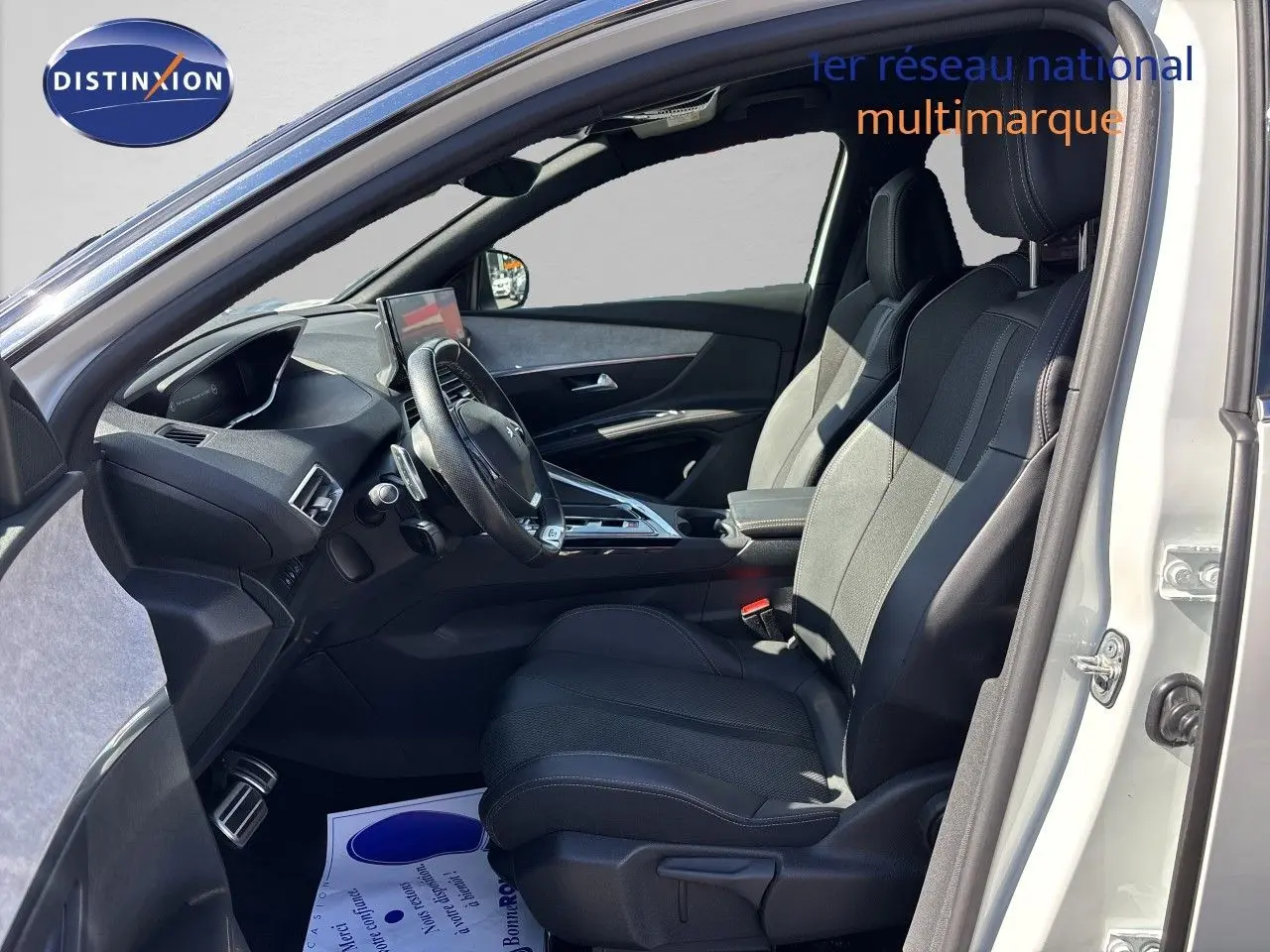 Intérieur côté conducteur d’un Peugeot 5008 blanc nacré 2023, sièges noirs en cuir et tableau de bord moderne.