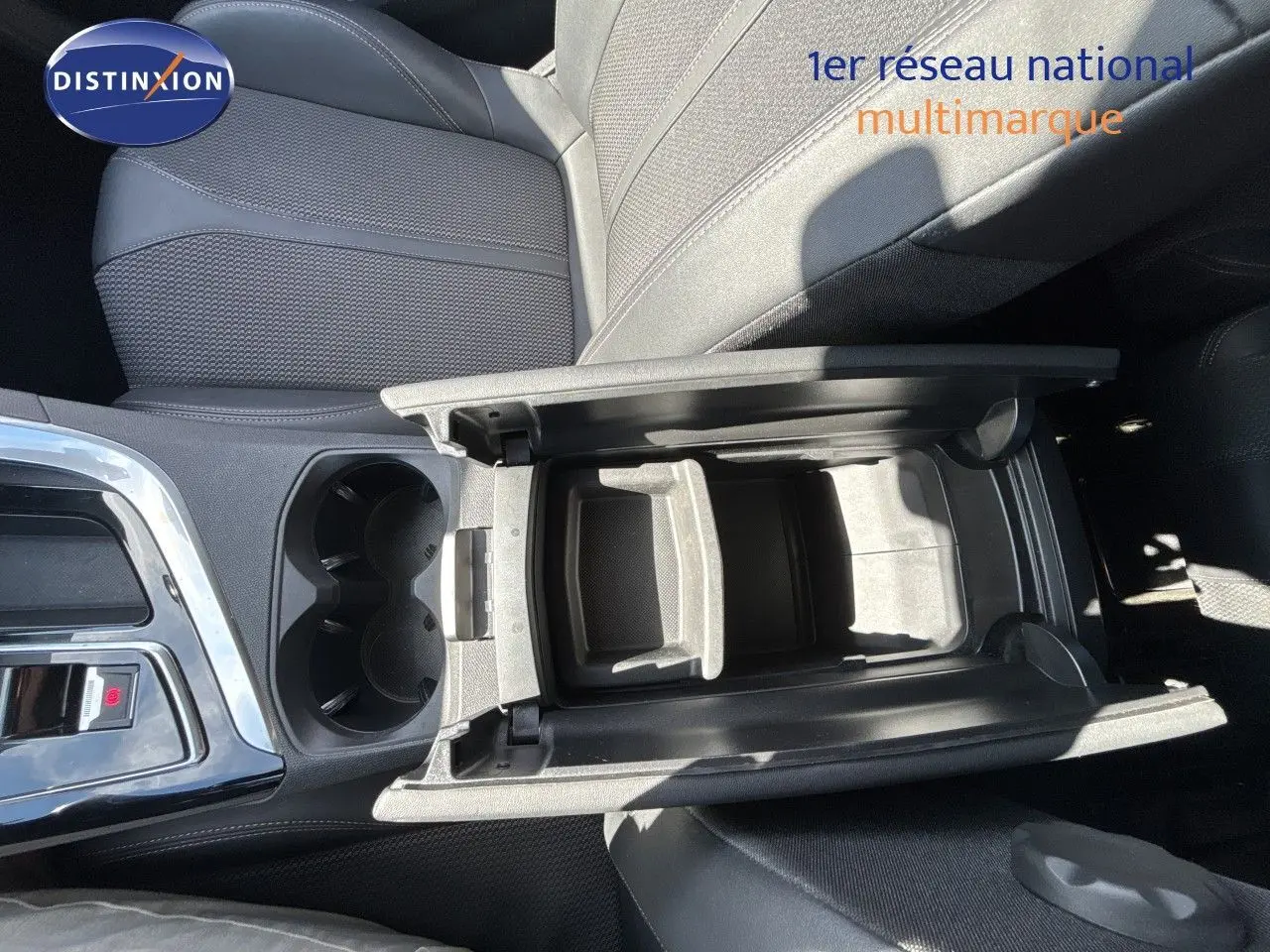 Vue plongeante sur l'accoudoir central ouvert et les sièges noirs en tissu du Peugeot 5008 Blanc Nacré 2023.