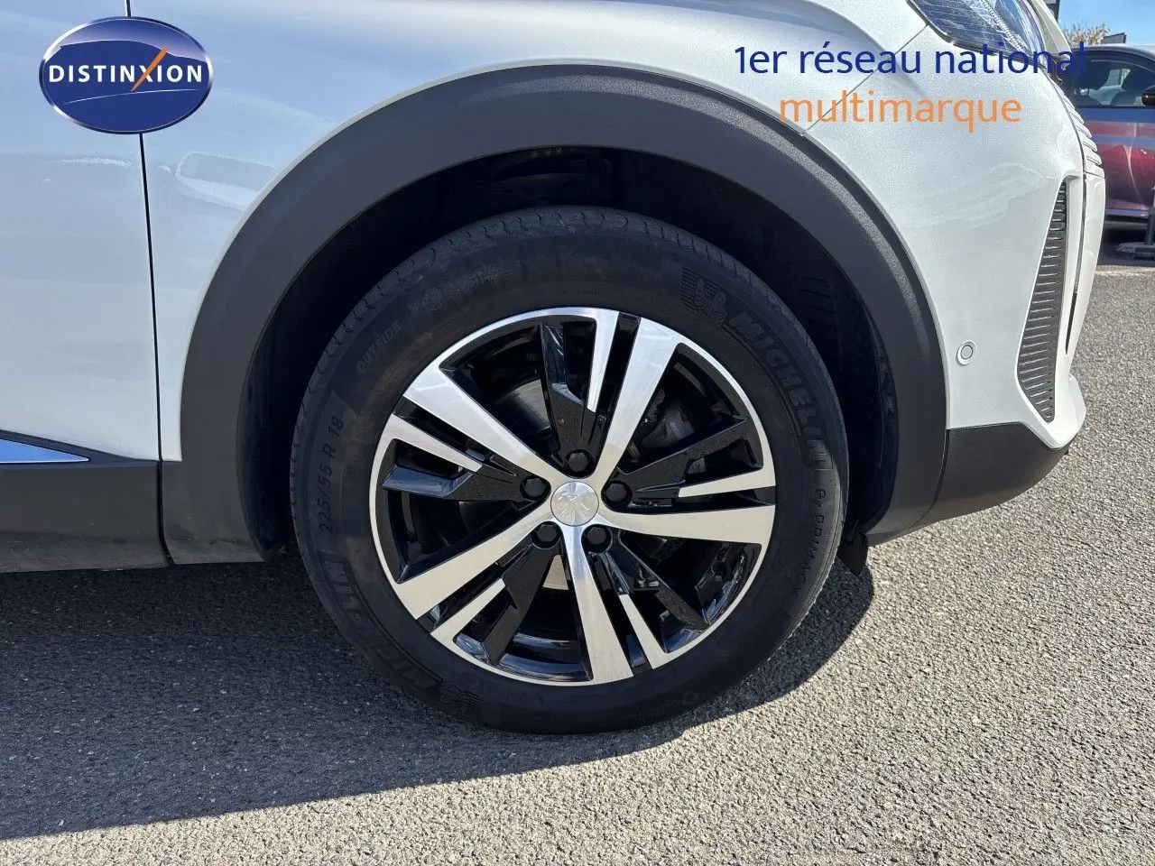 Gros plan sur la roue avant droite d’un Peugeot 5008 blanc nacré, mettant en valeur la jante alliage bicolore.