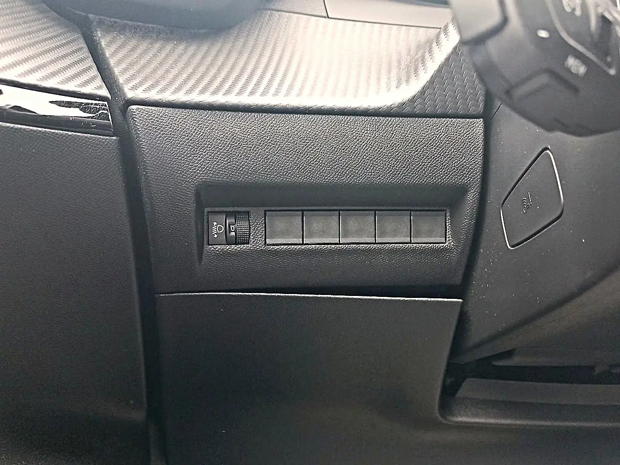 Détail intérieur côté gauche du tableau de bord noir avec commande de réglage des phares sur Peugeot 2008 rouge Elixir.