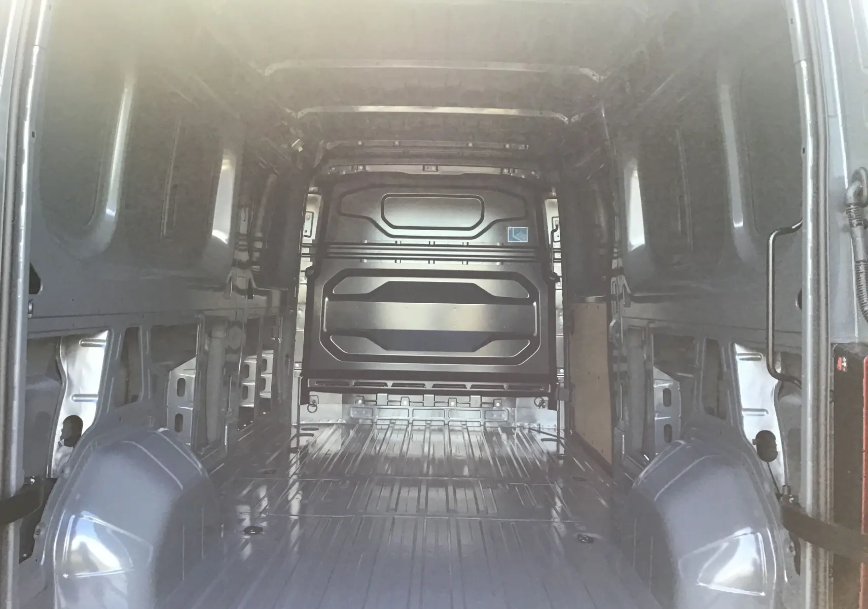 Vue intérieure arrière du Renault Master L3H2 gris urbain, montrant l'espace de chargement vide et la cloison métallique.