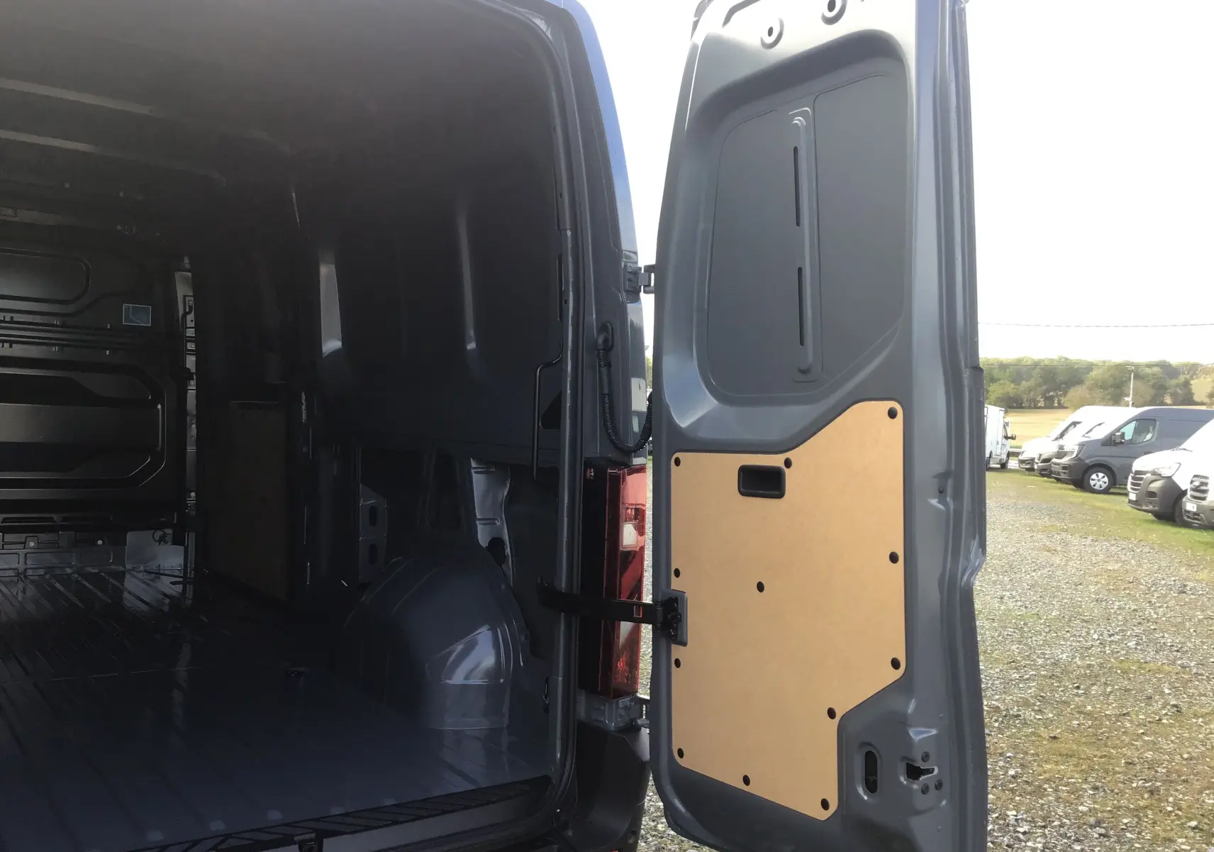 Vue arrière droite du Renault Master gris urbain 2025 avec porte ouverte montrant l'intérieur vide et le panneau bois de la porte.