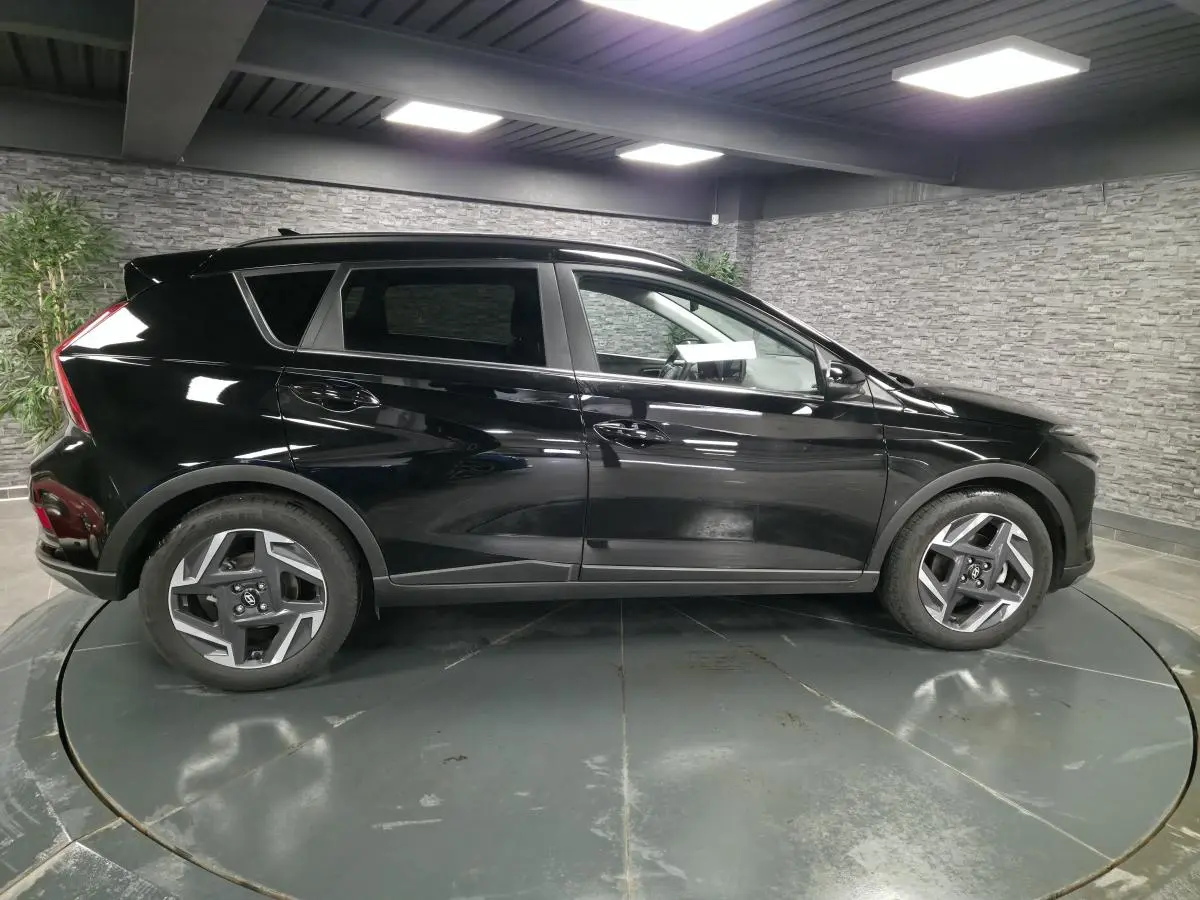 Profil côté gauche d'un Hyundai Bayon noir brillant, avec jantes alliage 17 pouces, dans un showroom intérieur.