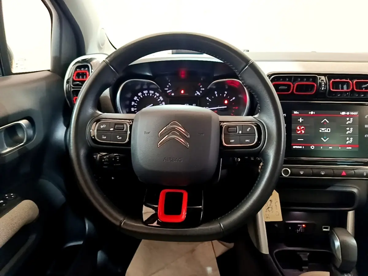 Vue intérieure centrée sur le volant cuir noir avec insert rouge et tableau de bord numérique du Citroën C3 Aircross.