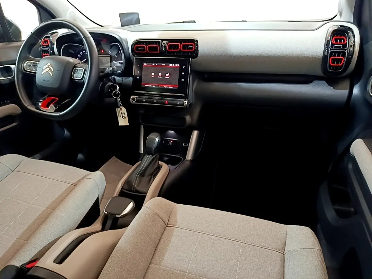 Intérieur avant du Citroën C3 Aircross 2020 avec tableau de bord noir, touches rouges sur aérateurs et sièges tissu gris clair.