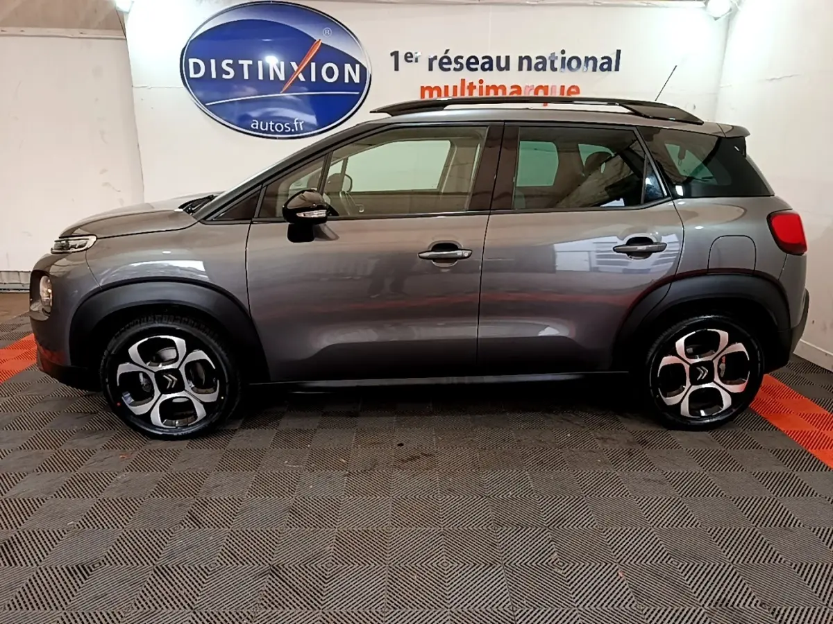 Profil côté gauche d'un Citroën C3 Aircross gris métallisé 2020 avec toit noir et jantes distinctives en intérieur showroom.