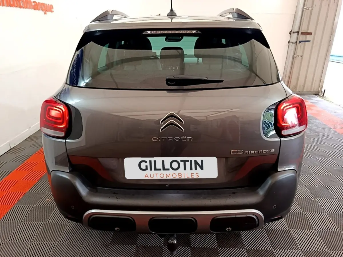 Vue arrière d'un Citroën C3 Aircross gris avec feux allumés et attelage dans un garage.