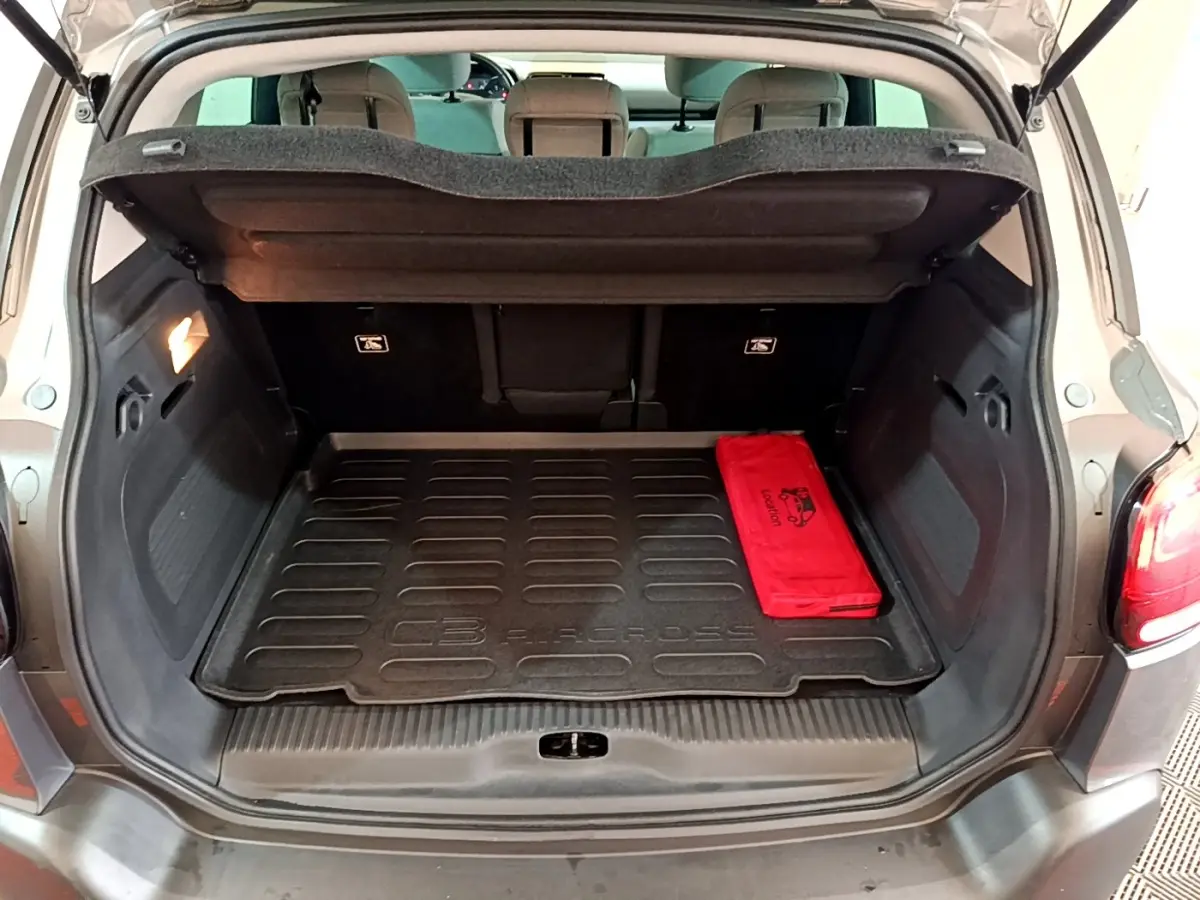 Coffre ouvert vu de l'arrière d'un Citroën C3 Aircross gris avec tapis de coffre noir et trousse rouge.
