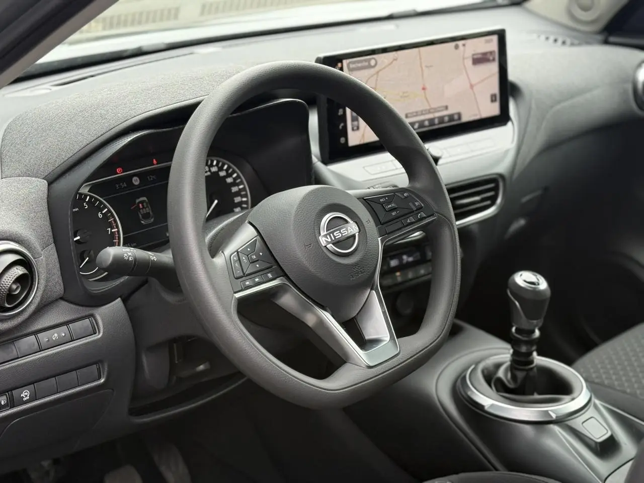 Vue intérieure centrée sur le volant Nissan et la console avec levier de vitesses manuelle et écran GPS tactile.
