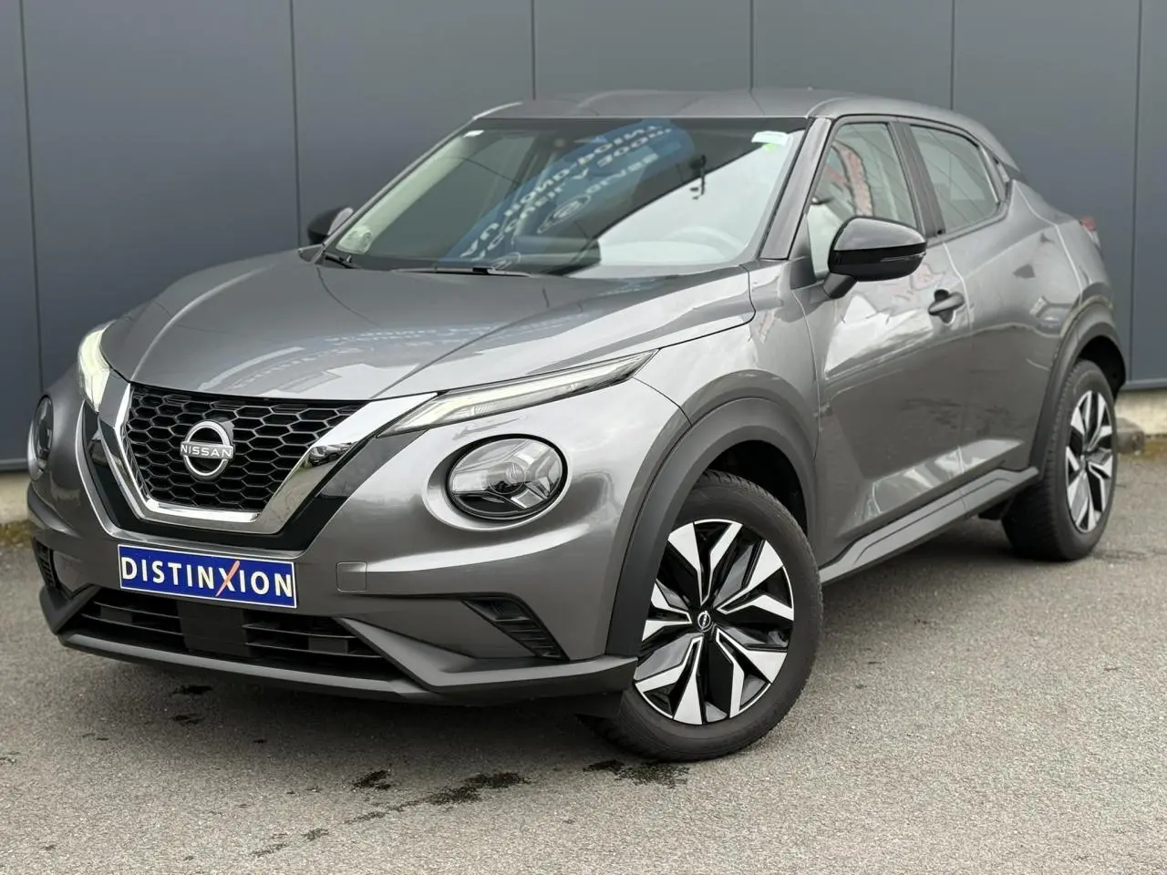 Nissan Juke gris foncé en vue 3/4 avant droit, mettant en valeur sa calandre V-Motion et ses phares LED distinctifs.