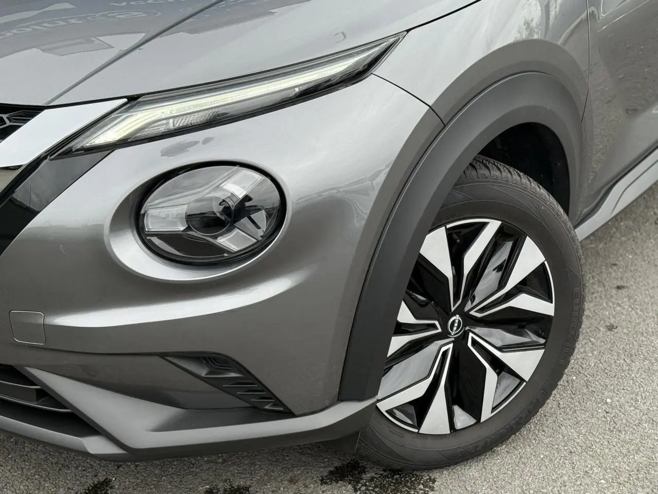 Gros plan sur l'avant droit du Nissan Juke 2025 gris foncé, mettant en valeur le phare rond et la jante bicolore.