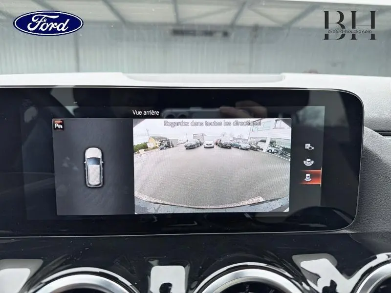 Écran multifonction montrant la caméra de recul d'une Mercedes Classe B noire cosmos, vue arrière en parking.