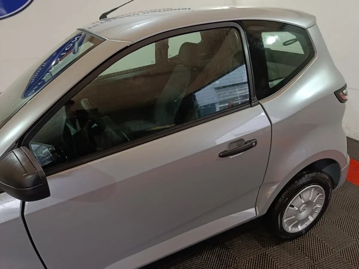 Vue côté gauche d'une Aixam Ambition 0.5 City Pack gris clair 2026 avec rétroviseur caméra conducteur et jantes argentées.