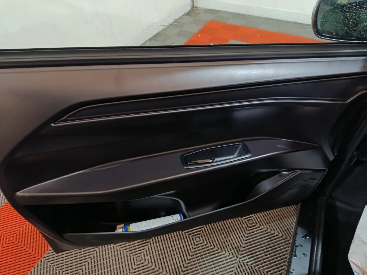 Vue intérieure sur la porte côté conducteur d'une Aixam Ambition gris clair, avec poignée et rangement bas visible.