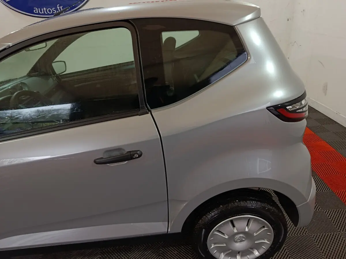 Vue latérale côté droit d'une Aixam Ambition 0.5 City Pack gris clair, mettant en valeur la porte arrière et le feu arrière.