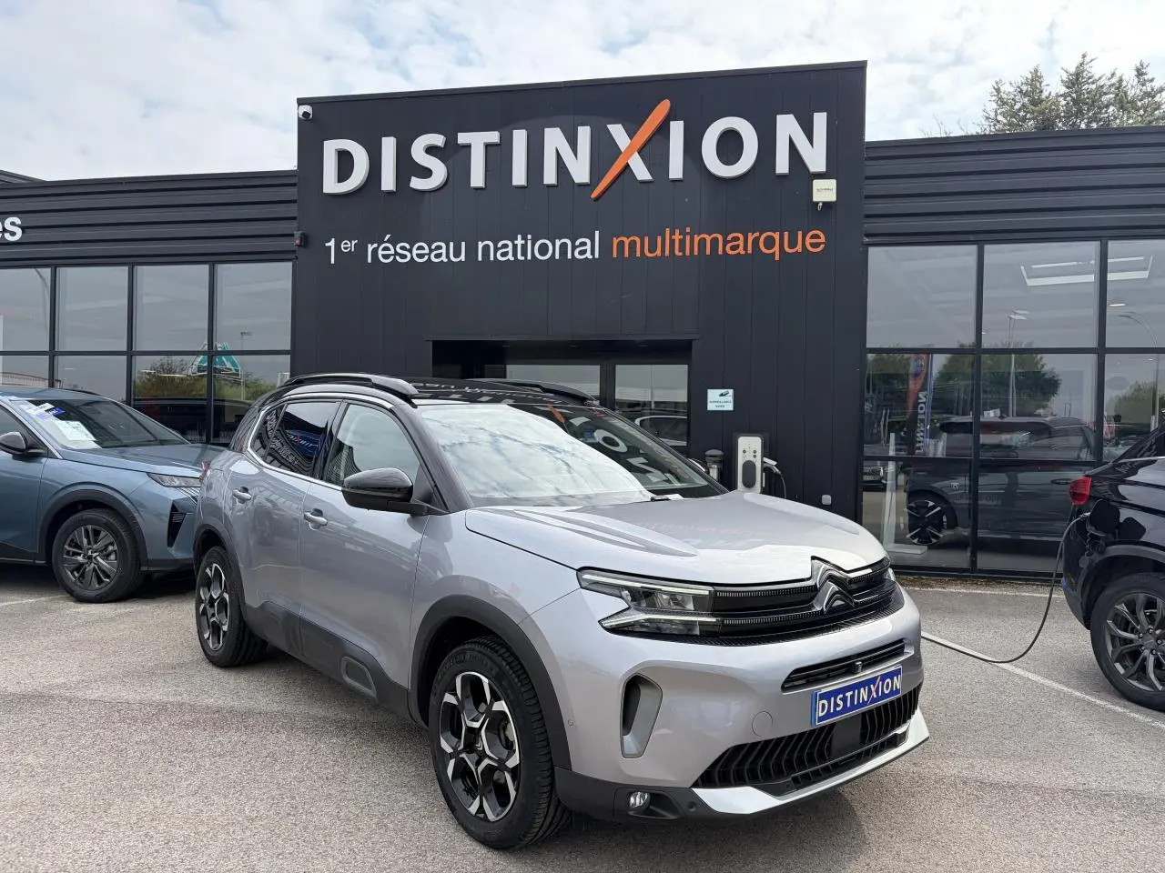 Vue 3/4 avant droit d’un Citroën C5 Aircross gris métal avec toit noir et jantes alliage bi-ton devant un concessionnaire.