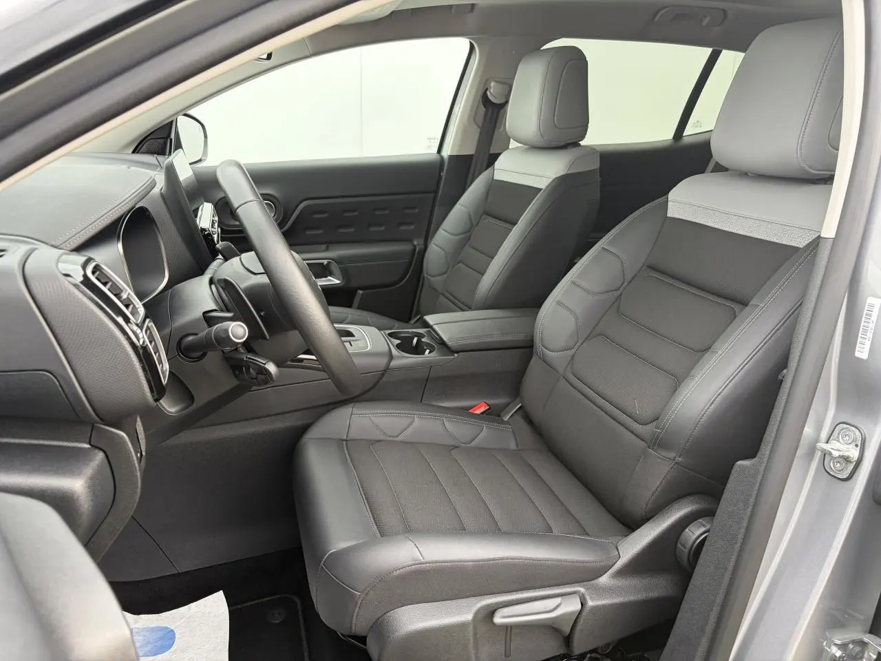 Vue intérieure côté conducteur du Citroën C5 Aircross 2024 gris métal, sièges bi-ton gris avec volant cuir et console centrale.