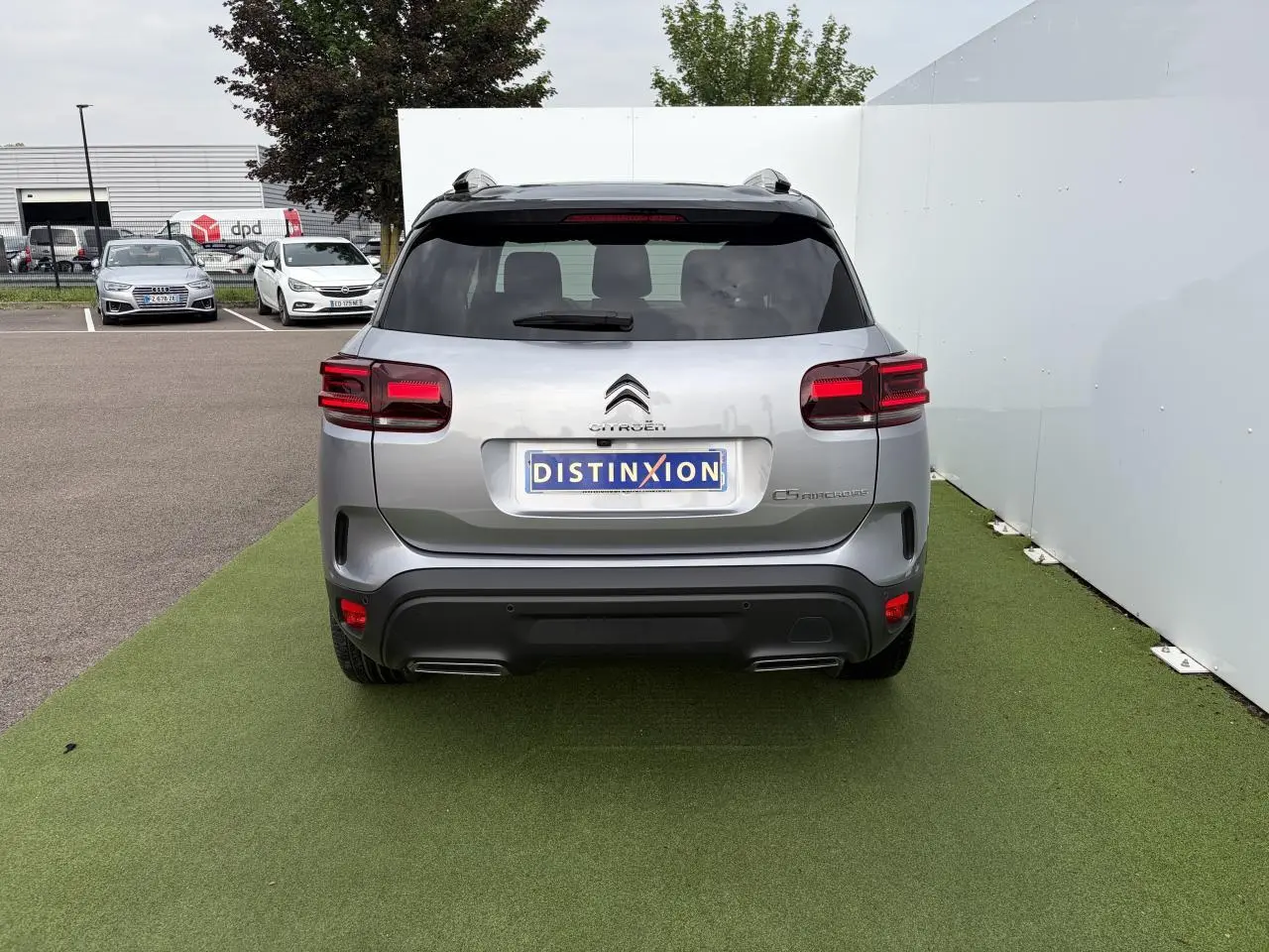 Vue arrière d'un Citroën C5 Aircross gris métal avec toit noir et feux arrière LED 3D, stationné sur sol vert.