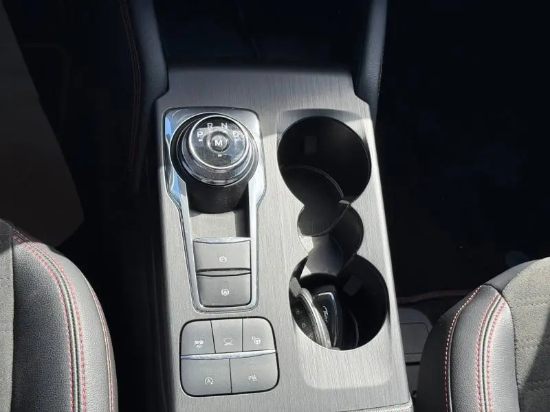 Vue plongeante sur la console centrale grise du Ford Kuga noir, avec molette de boîte auto et porte-gobelets.