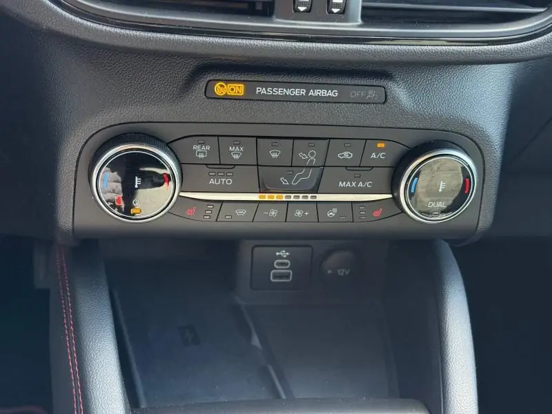 Vue rapprochée de la console centrale du Ford Kuga 2023, montrant les commandes de climatisation bi-zone et l'indicateur airbag passager.