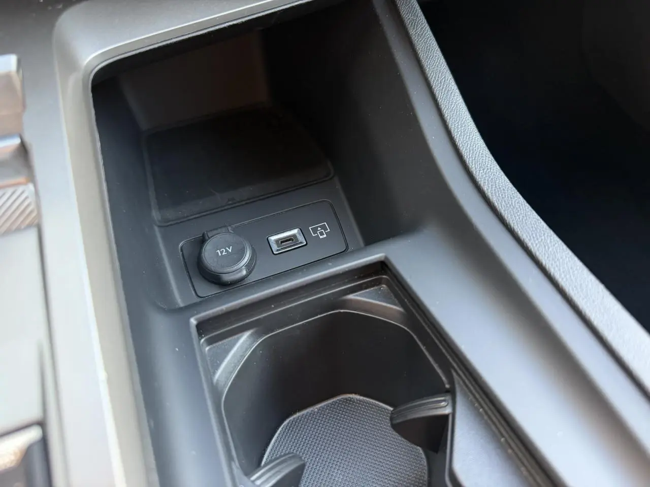 Gros plan sur la console centrale noire de la Peugeot 308 2025, montrant prise 12V et port USB.