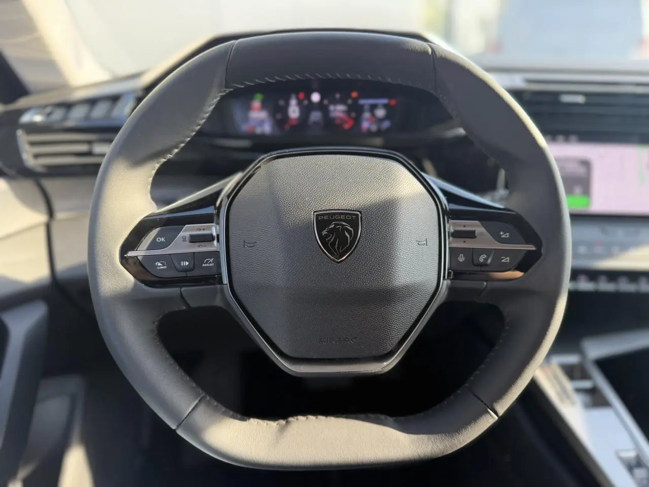 Vue rapprochée du volant cuir noir à méplat du Peugeot 308 2025 avec commandes intégrées et logo central.