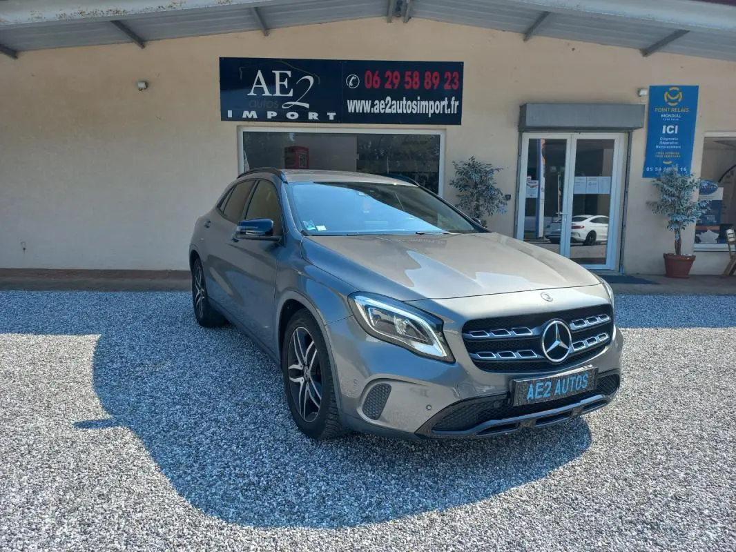 Mercedes GLA gris 3/4 avant droit, avec calandre distinctive et jantes alliage, stationné devant un bâtiment commercial.