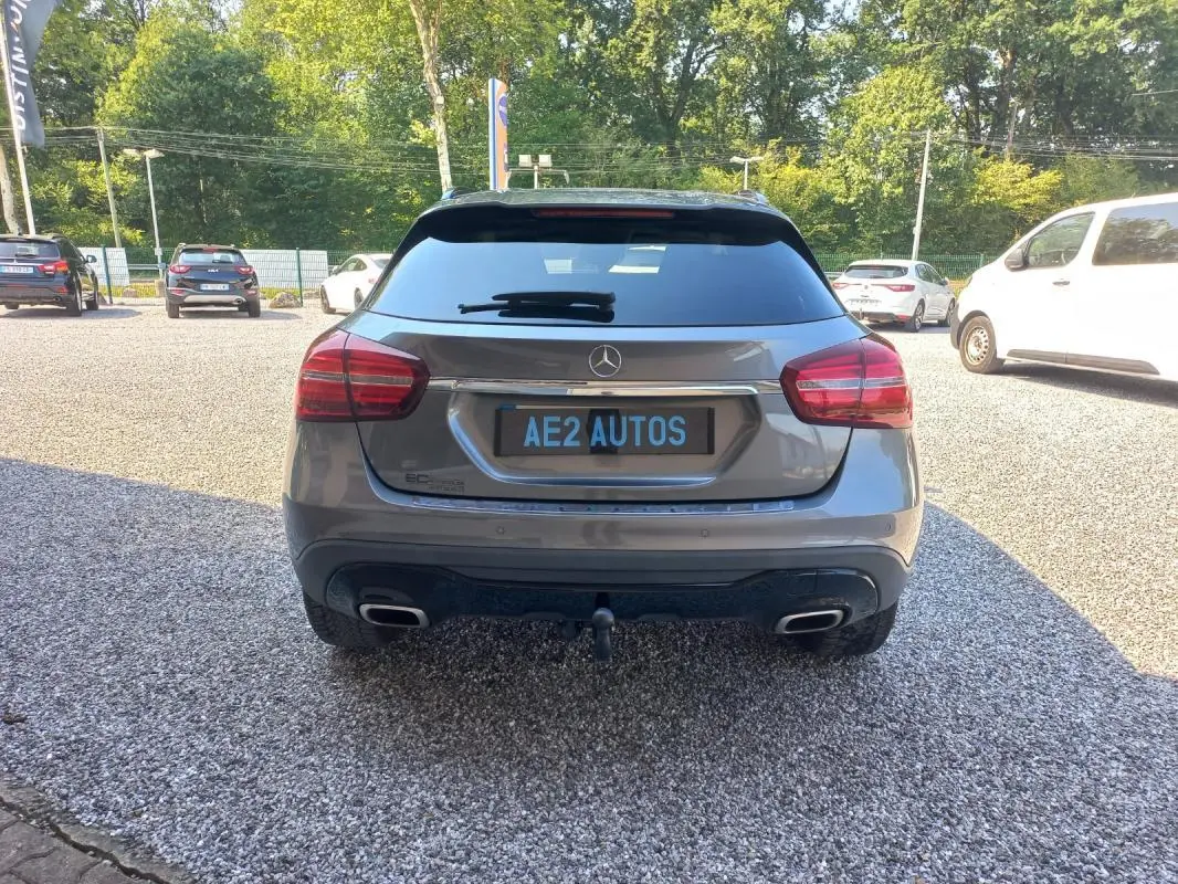 Vue arrière d'une Mercedes GLA gris 2019 avec double sortie d'échappement et attelage visible sur un parking extérieur.