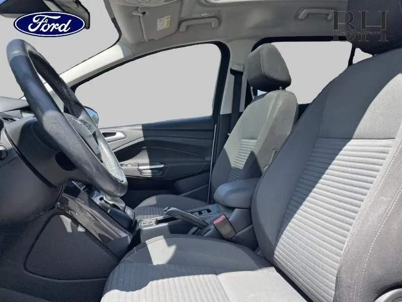 Vue intérieure côté conducteur du Ford Grand C-Max 2017, sièges tissu gris et volant cuir multifonction.