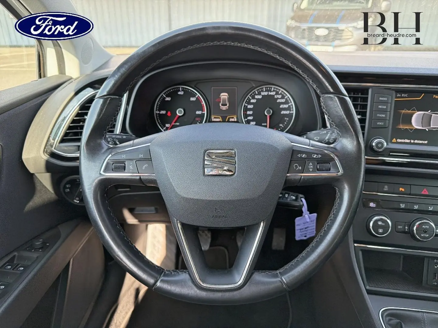 Volant cuir noir vu de face dans l'habitacle d'une SEAT LEON ST, avec tableau de bord et écran tactile visible.