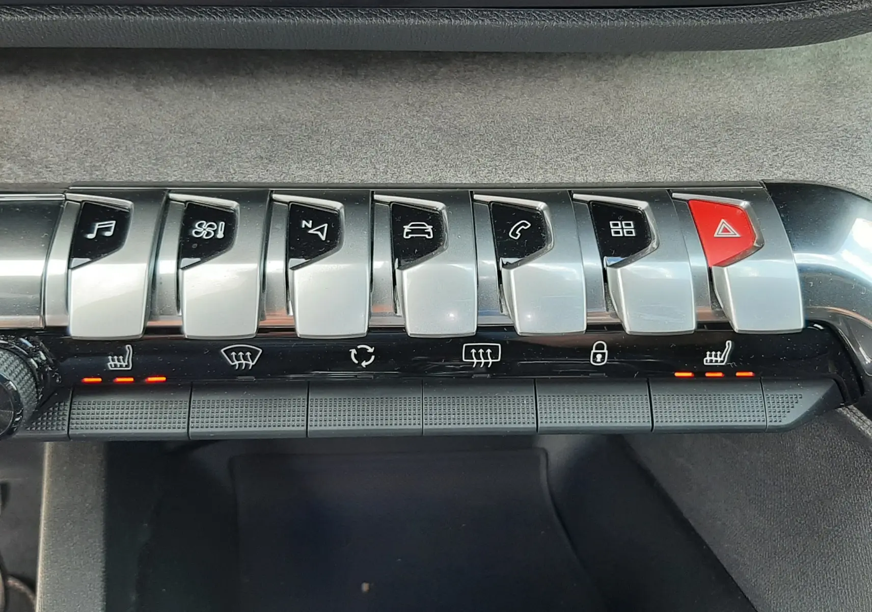 Gros plan sur la rangée de boutons argentés et noirs du tableau de bord du Peugeot 3008 blanc nacré, avec voyants rouges allumés.