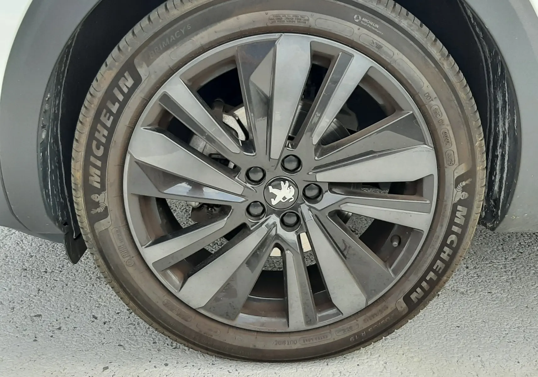 Gros plan sur la roue avant droite du Peugeot 3008 blanc nacré avec jante alliage gris foncé et logo lion central.