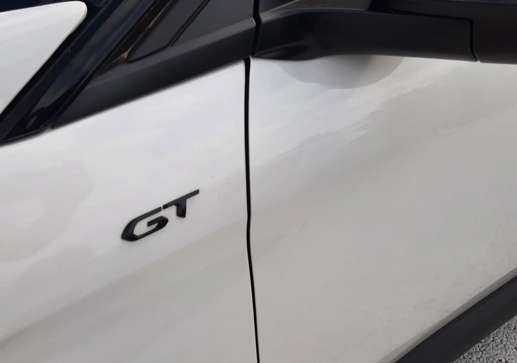 Détail du logo GT sur la porte avant gauche d’un Peugeot 3008 blanc nacré avec toit noir.