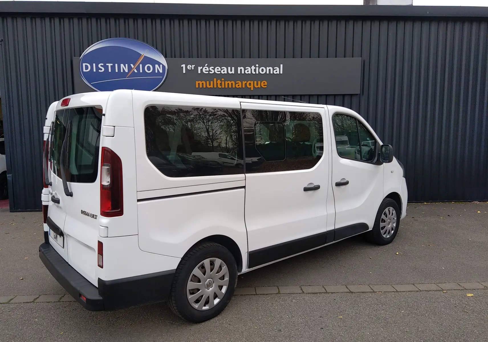 Renault Trafic Microbus blanc vu en 3/4 arrière droit, avec vitres teintées et hayon arrière fermé.