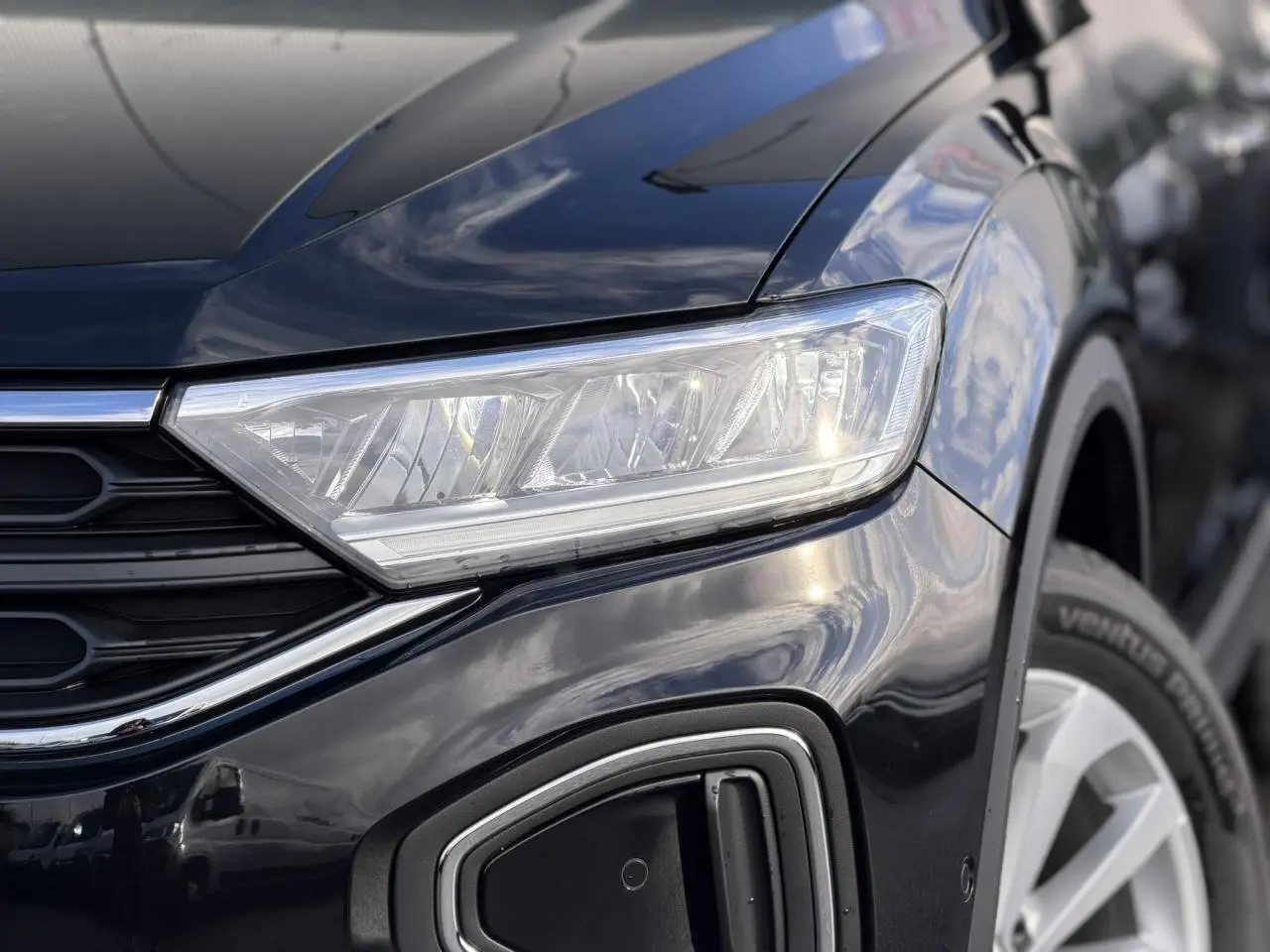 Gros plan sur l'avant droit du Volkswagen T-Roc Deep Black 2025, mettant en valeur le phare LED et la roue.