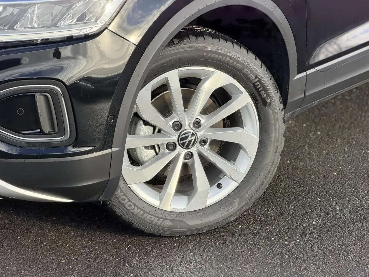 Gros plan sur la roue avant droite en alliage du Volkswagen T-Roc Deep Black avec partie avant du pare-chocs visible.
