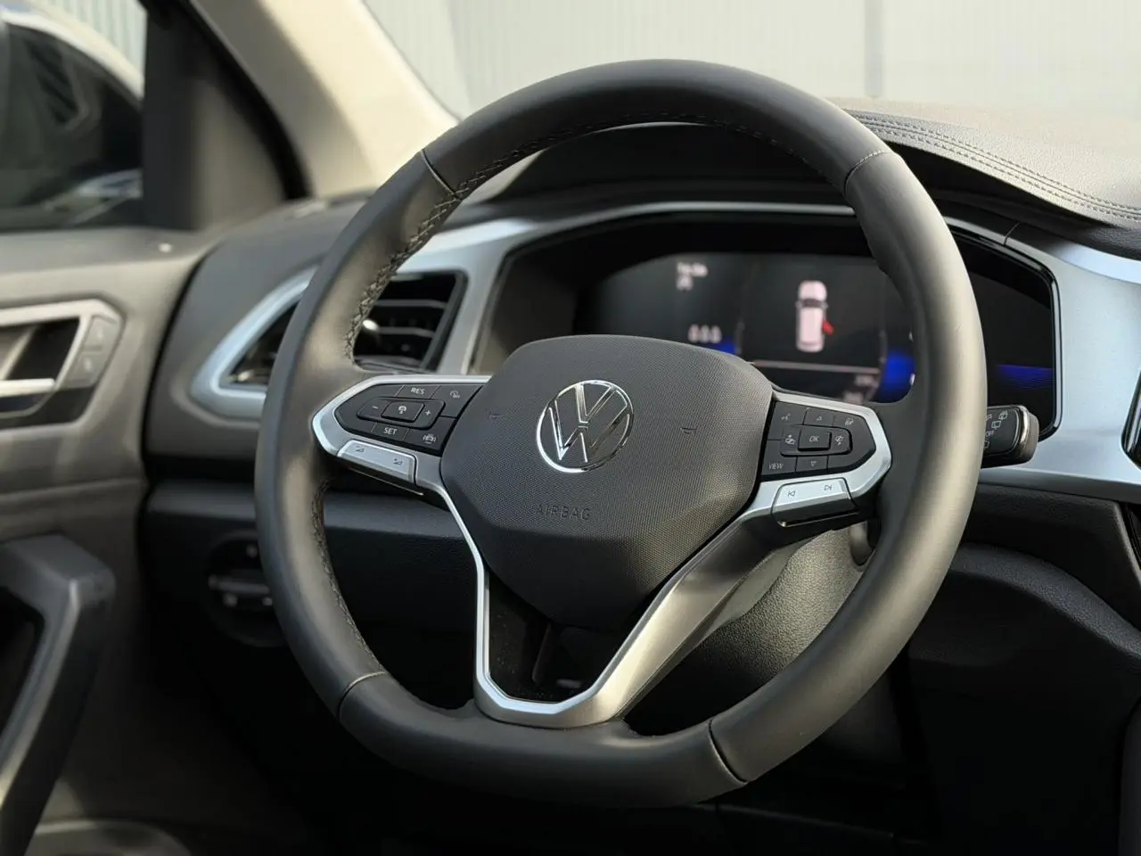 Vue rapprochée du volant cuir multifonction noir du Volkswagen T-Roc 2025 avec tableau de bord digital en arrière-plan.