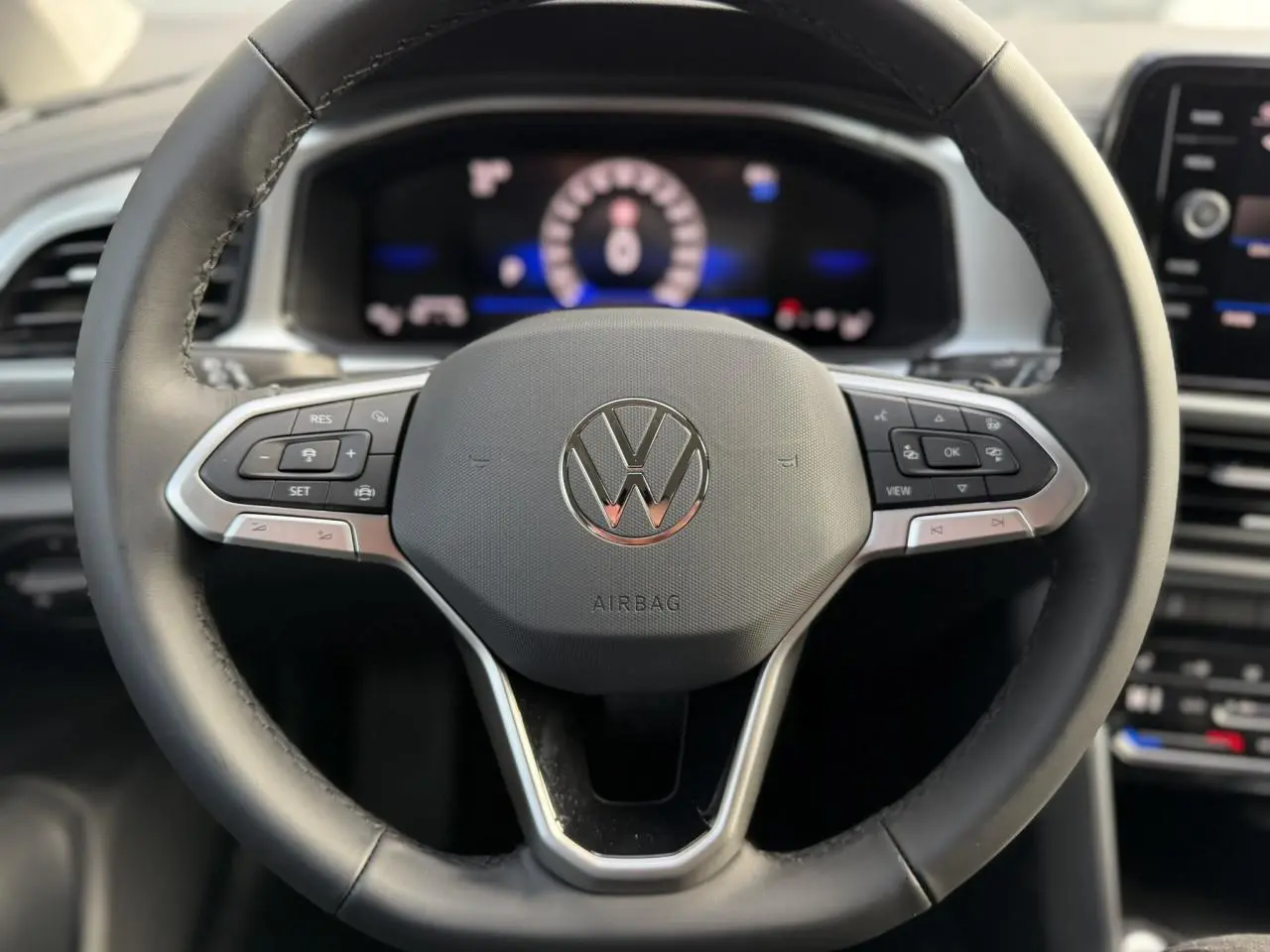 Gros plan sur le volant en cuir multifonction noir du Volkswagen T-Roc 1.5 TSI 150 DSG Life 30 Years, tableau de bord digital en arrière-plan flou.