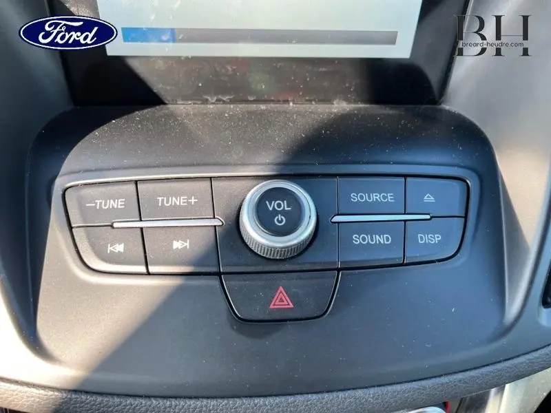 Gros plan sur les commandes audio centrales du tableau de bord du Ford Kuga 2018, boutons noirs avec molette volume.