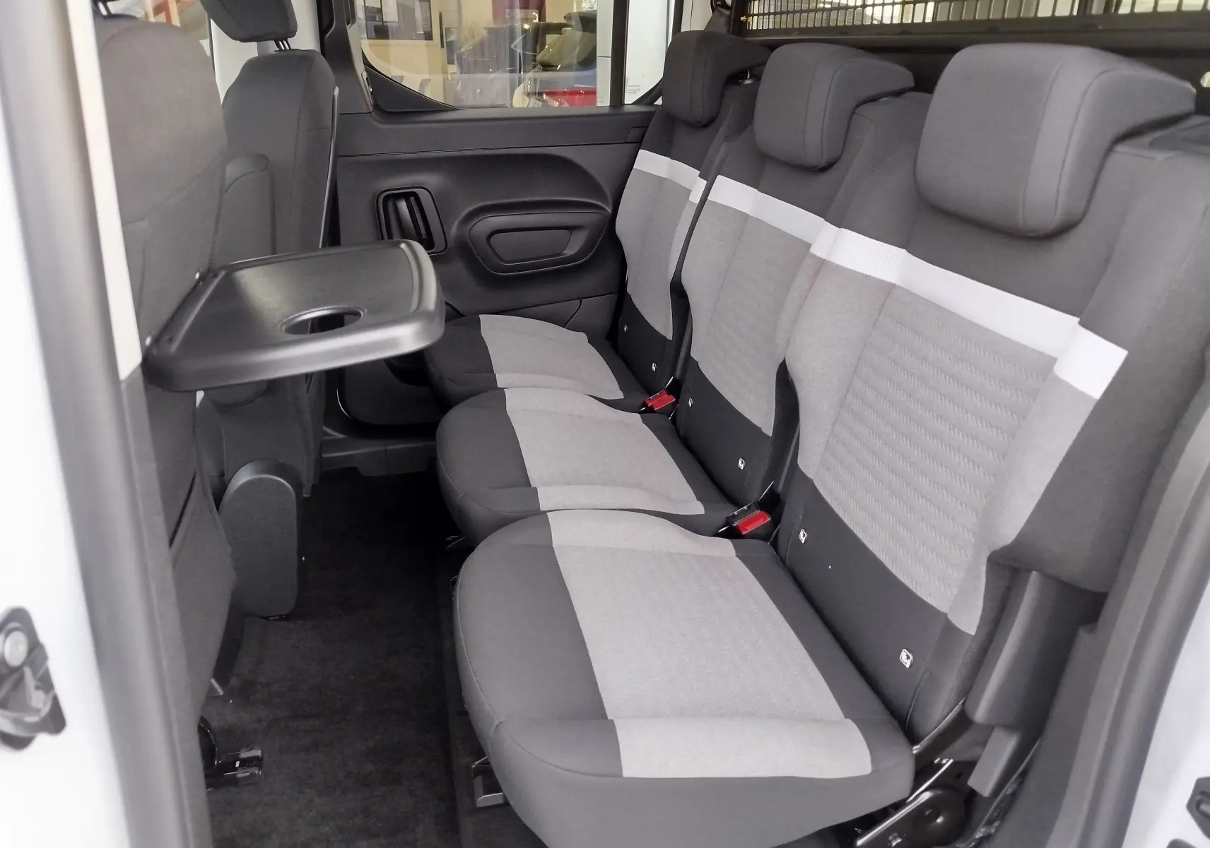 Vue intérieure côté droit du Citroën Berlingo 2025 Kaolin White, montrant la banquette arrière grise avec tablette rabattable.