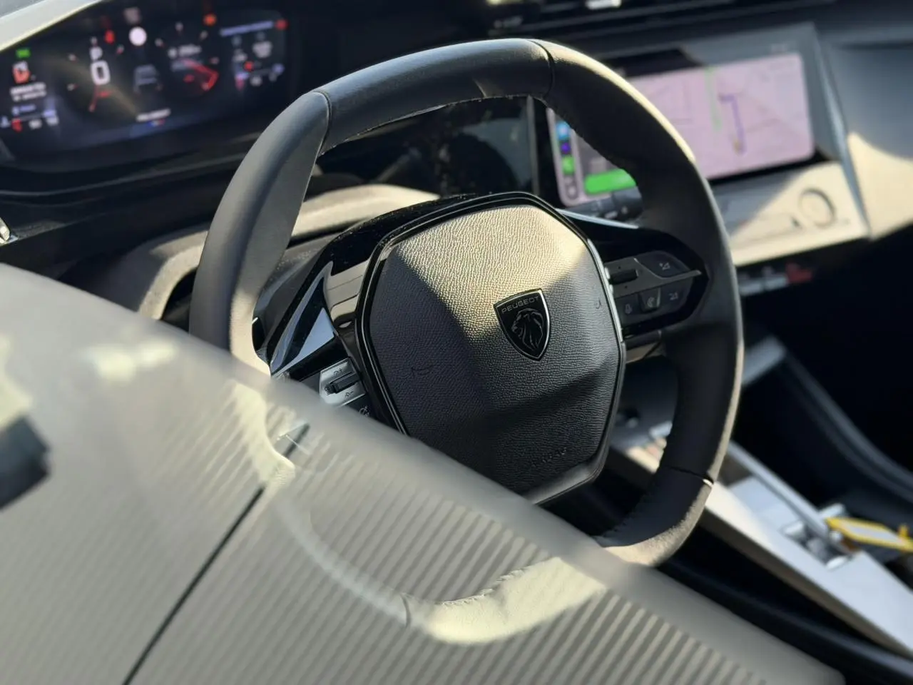 Gros plan sur le volant cuir noir de la Peugeot 308 2025, avec tableau de bord numérique et écran tactile en arrière-plan.