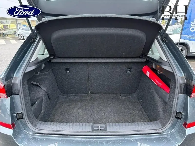 Coffre ouvert vu de l'arrière d'un Skoda Kamiq gris Météore avec tapis et rangement latéral visible.
