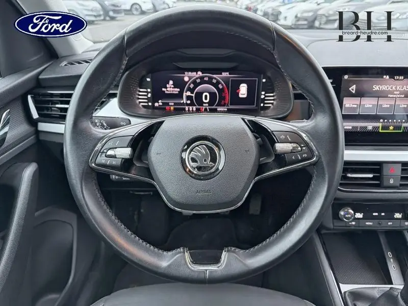 Vue intérieure centrée sur le volant cuir multifonction d’un Skoda Kamiq gris, avec tableau de bord numérique et écran tactile visible.