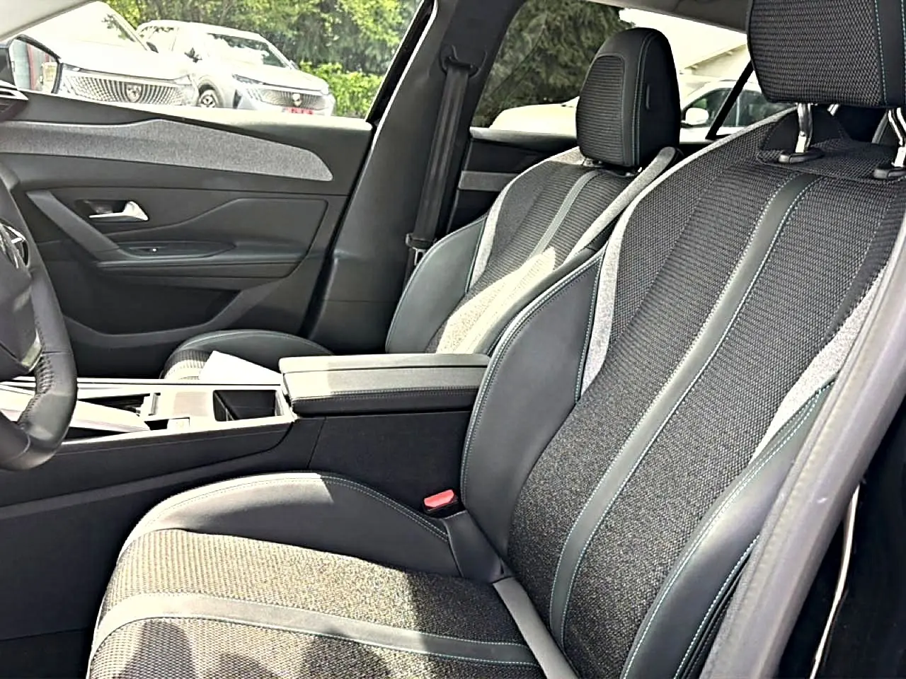 Vue intérieure côté gauche des sièges avant en tissu et cuir gris avec accoudoir central sur Peugeot 408 Hybrid 2024.