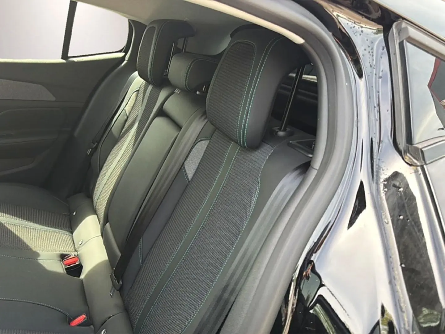 Vue intérieure côté droit sur la banquette arrière noire avec surpiqûres vertes d'une Peugeot 408 Hybrid 2024.