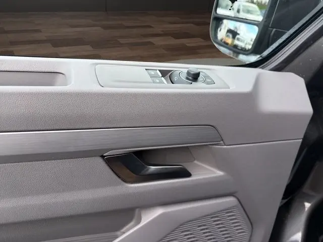 Détail de la porte côté conducteur du Volkswagen Transporter gris foncé, avec commandes des rétroviseurs et poignée intérieure noire.