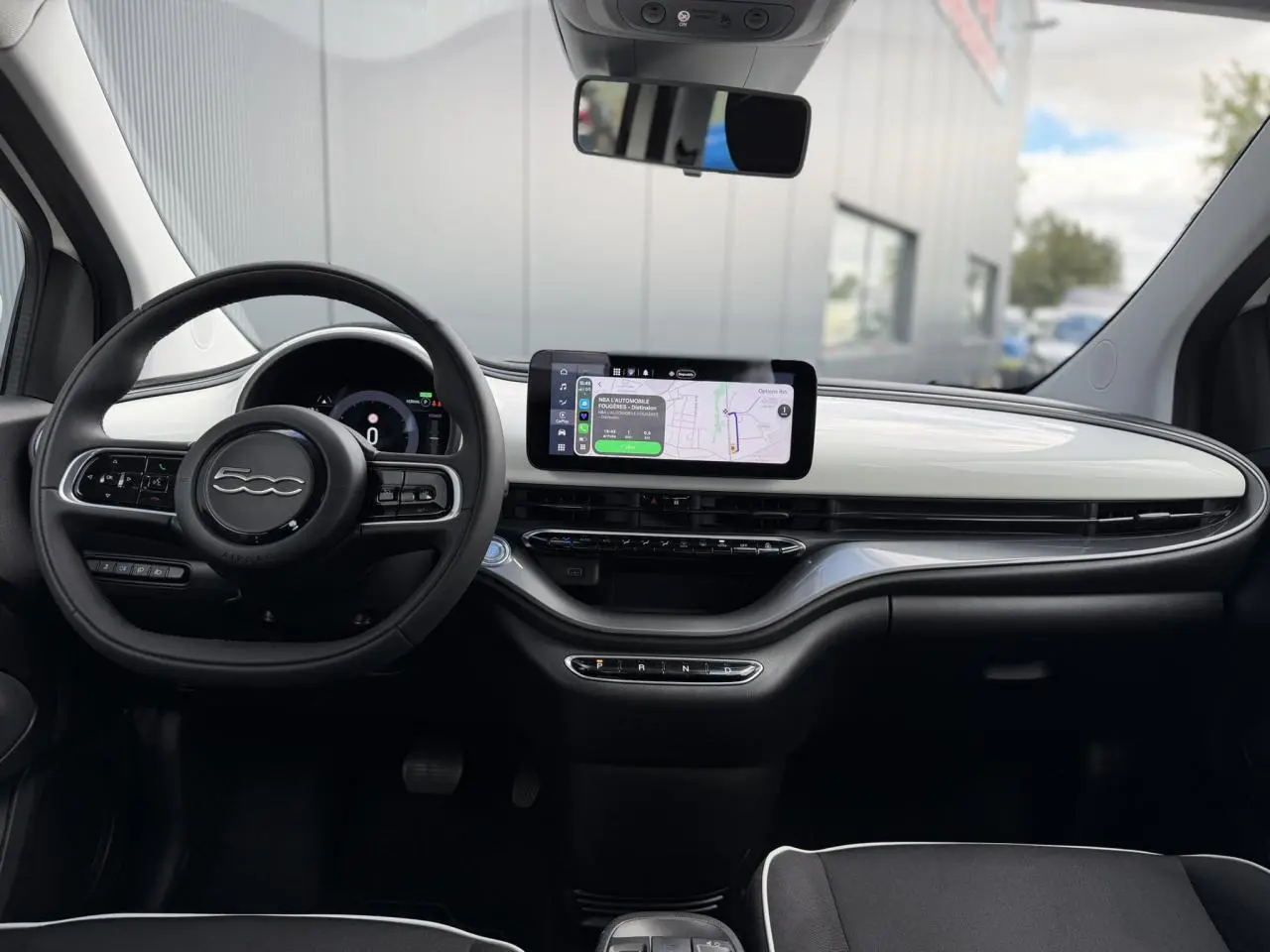 Vue intérieure du tableau de bord blanc Artic de la Fiat 500 électrique 2024 avec écran tactile central et volant noir Soft-Touch.