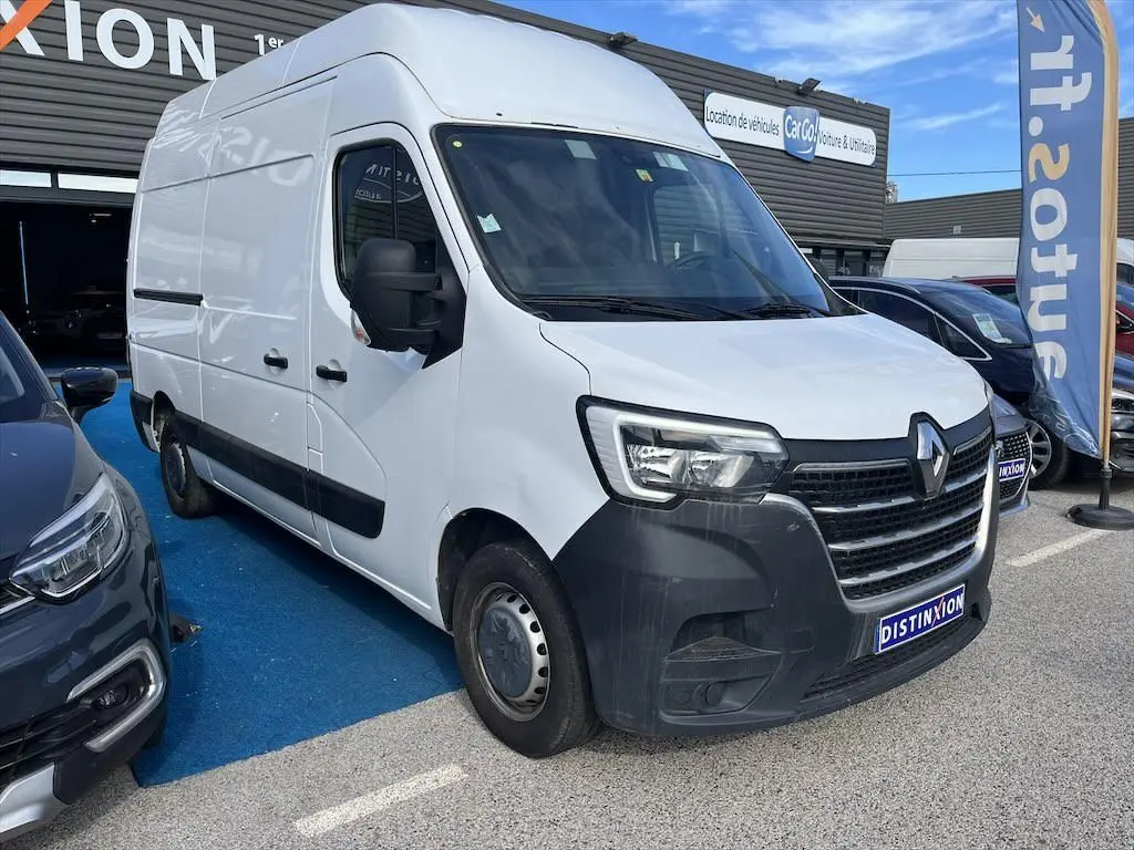 Vue 3/4 avant d’un utilitaire Renault Master blanc avec pare-chocs noir, stationné sur un parking extérieur.