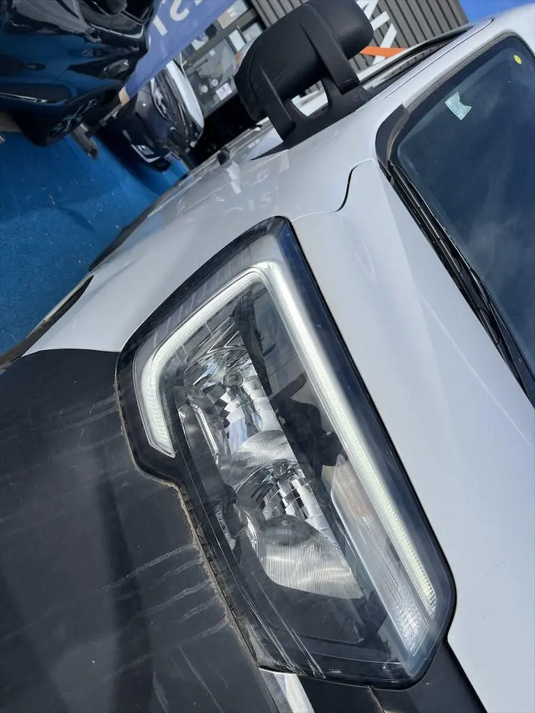 Gros plan sur le phare avant droit du Renault Master blanc, soulignant le capot et le rétroviseur noir.