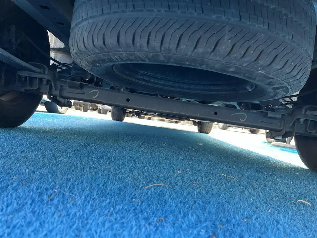 Vue en contre-plongée sous un Renault Master blanc, montrant la roue de secours suspendue et le châssis arrière.